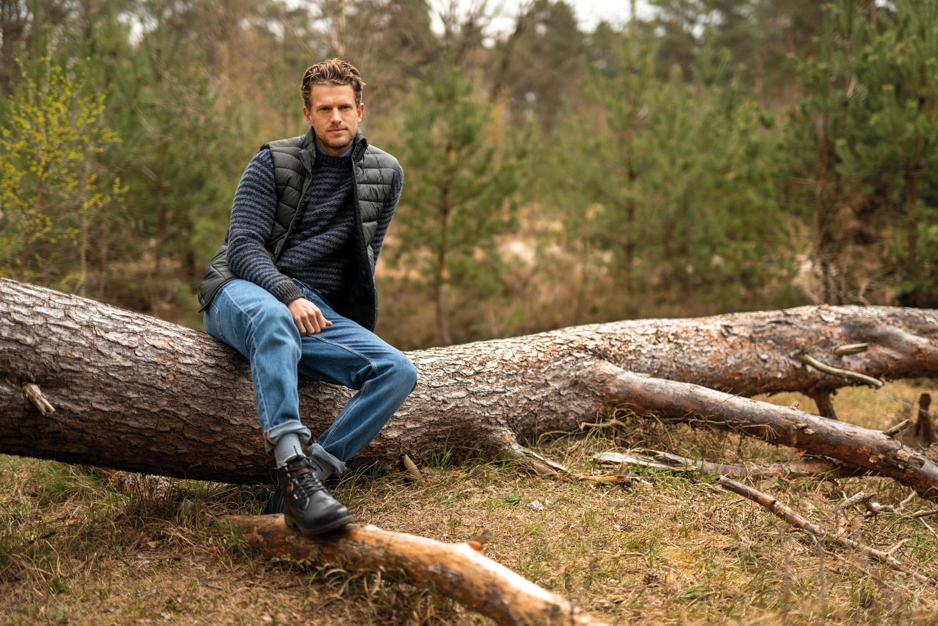 Ein Mann sitzt mit Schuhen auf einem Baustamm im Wald